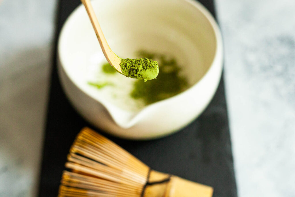 Matcha w proszku na bambusowej miarce chashaku z trzepaczką chasen w tle